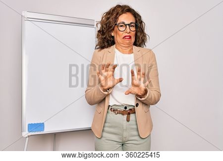 Middle age senior business woman standing on seminar presentation by magnectic blackboard disgusted expression, displeased and fearful doing disgust face because aversion reaction.