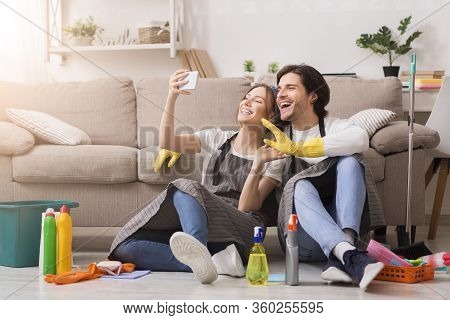 Quarantine Pass Time. Smiling Young Couple Taking Selfie On Smartphone After Spring-cleaning Apartme