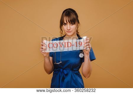 A Doctor In A Mask, Gloves And With A Stethoscope Holds The Inscription Covid-19 In His Hands.