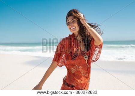 Beautiful latin woman running on tropical beach with copy space. Happy glamour and carefree woman walking on beach while looking behind. Stylish girl with black bikini enjoying summer vacation at sea.