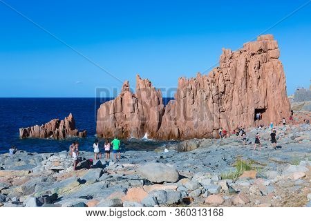 Sardegna, Italy - July 2019:
Sardinia Coastline: Typical Red Rocks And Cliffs And Tourists Near Sea 