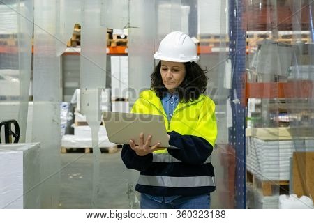 Focused Female Engineer Using Laptop Computer Onsite. Middle Aged Woman In Hardhat And Uniform Stand