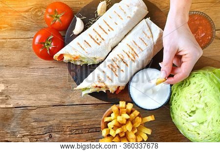 Shawarma Sandwich  With French Fries On The Cuisine Table. Hand Puts Fried Potato Into The Sauce.