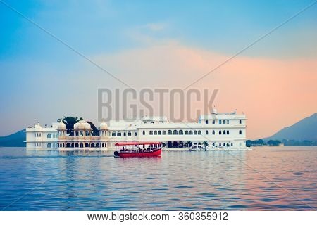 Romantic luxury India travel tourism - tourist boat in front of Lake Palace (Jag Niwas) complex on Lake Pichola on sunset with dramatic sky, Udaipur, Rajasthan, India