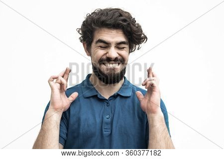 Excited Joyful Guy Keeping Fingers Crossed, Making Wish. Handsome Bearded Young Man In Blue Casual T