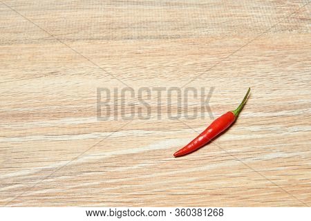 Background - A Lone Pod Of Red Chili Peppers Lies On A Wooden Surface