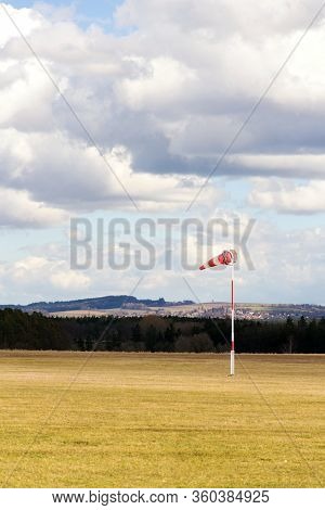 Red And White Windsock On Empty Grassy Airfield, Dramatic Clouds In Background, Windy Weather Foreca