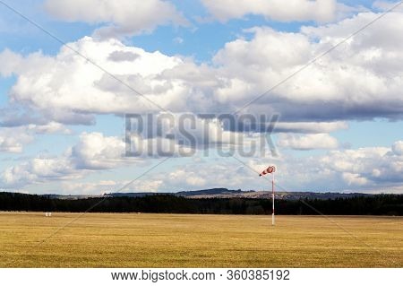 Red And White Windsock On Empty Grassy Airfield, Dramatic Clouds In Background, Windy Weather Foreca