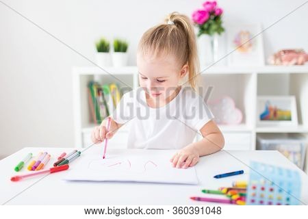 Blonde Happy Little Girl With Ponytale Drawing And Writing Lsitting By The White Table In Light Roon