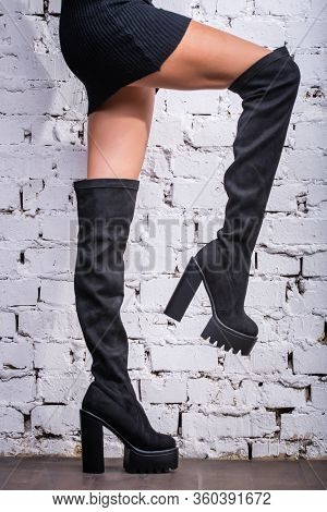 Black Hessian Boots On The Feet Of A Model On A White Brick Background. Jackboots. Studio Shooting. 