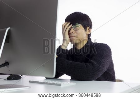 Asian Overworked Men In Glasses Sitting In Office, Looks Exhausted, Tired Of Work. Hand Covers Face.
