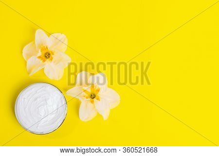 Flowers Head Of Daffodil And Cosmetic Cream In Jar On Bright Yellow Background. Skin Care Concept Wi