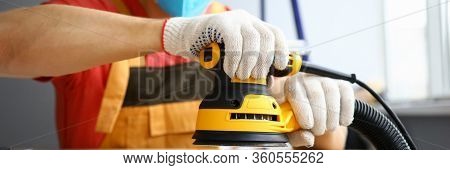 Close-up Of Male Worker Holding Sander Machine And Working With Wood. Handyman Wearing Protective Ye