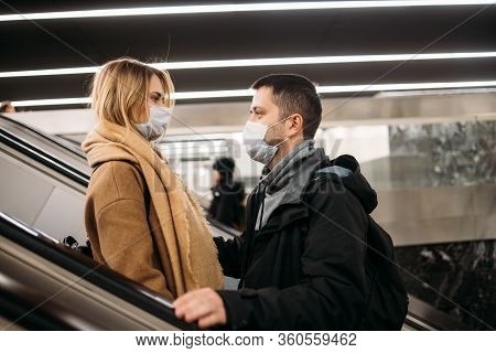 Side View Of Loving Couple In Medical Masks On Escalator In Subway. Coronavirus Pandemic.
