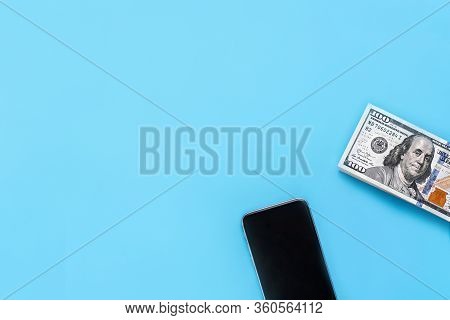 Mobile Phone And Us Dollar Bills On A Blue Background. Concept Of Payment Via Mobile Phone. Payment 