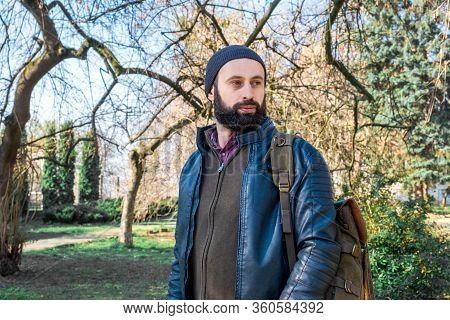 Adult Bearded Man With Backbag Walks Through The Spring Park In The Morning.