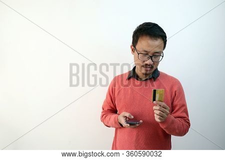 A Man Looking At His Credit Card And Smartphone In A Confused Face. E Commerce And Payment Concept I