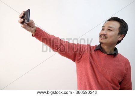 A North East Indian Manipuri Guy Taking Selfie Photograph In A Mobile Phone Isolated In White Backgr