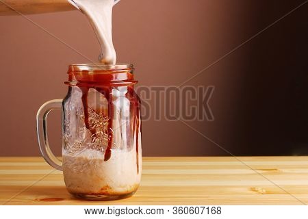 Milkshake Making On Wooden Table Closeup. Process Of Topping And Decorating Milkshake. Desset With C