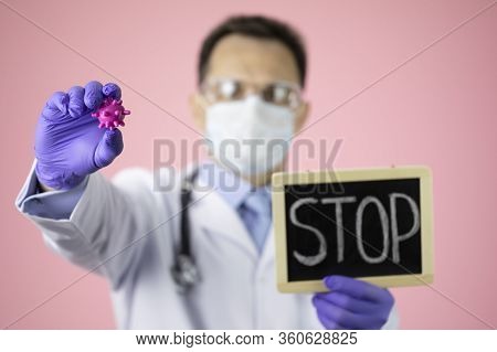 Male Doctor In Medical Uniform, Protective Mask And Glasses Holding Covid-19 Virus Cell And Stop Sig