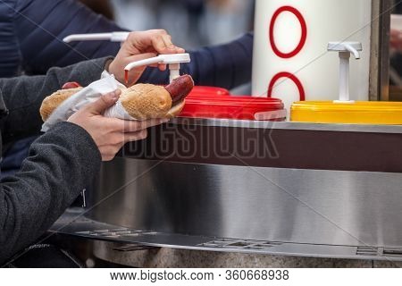 Hands Of A Woman Pouring Sauces, Ketchup And Mustard, On A Hot Dog Made Of Prague Sausage, Or Vaclav