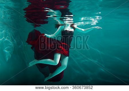 Beautiful Girl In A Red Dress Swims Under Water. Amazing Underwater Beauty Photo. Dive Under The Wat