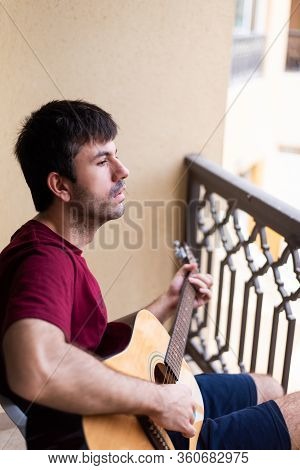 Man Playing Guitar On The Balcony While Spending Time At Home Practicing Social Distancing