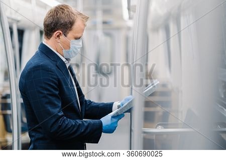 Sideways Shot Of Young Elegant Man Reads Newspaper Attentively, Poses In Metro Carriage, Wears Medic