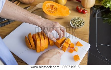 Man Cutting Fresh Raw Pumpkin For Preparing Vegan Soup Or Pie For Lunch In The Kitchen, Copy Space