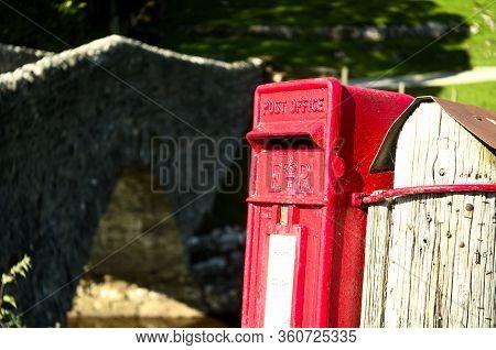 Bright Red Postbox Clings To A Post By A Rural Bridge In Yorkshire
