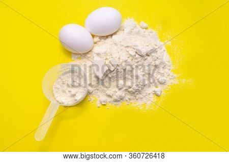 Heap Of Protein Powder With Plastic Spoon And Two Egg On Yellow Background