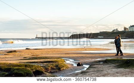 Panoramic View Of Couple Walking On The British Seaside At Sunset In Tynemouth, United Kingdom