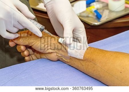 Doctor Push Syringe In Heparin Plug Hand Of Patient