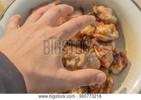The Hand Of A Man Reaches For Fried Meat Lying In A Bowl