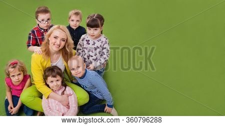 Group Of Children Boys And Girls Hug Teacher. Children Lovingly Hug Their Teacher In Kindergarten Or