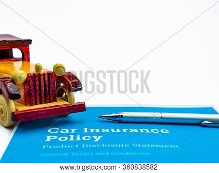 A Silver Ball Pen And One Wooden Vintage Toy Car Over Blue Insurance Papers Shot Against White Backg