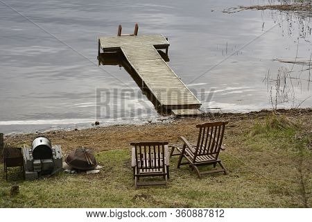 Southern Karelia, Finland, May, 10, 2014. Lake Waterside With Dock. Green Grass On The Shore. Two Wo