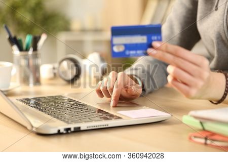 Close Up Of Student Girl Hands Paying Online On Laptop With Credit Card Sitting On A Desk At Home