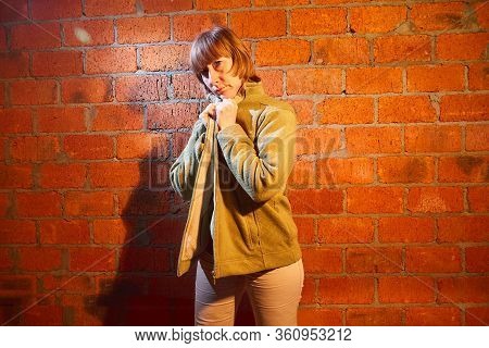 A Middle-aged Woman Poses Showing Clothes Near Red Brick Wall. An Inept Model In An Inept Shoot