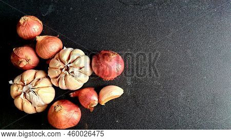 Bunch Of Onions And Garlic On A Black Table Board.