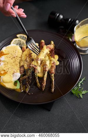 Baked Aspargus Covered With Bacon And Poached Eggs On A Black Ceramic Plate