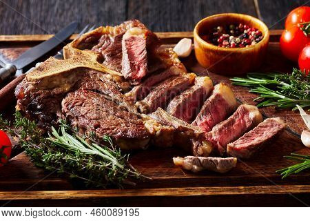 Roast Sliced Porterhouse Steak, T-bone Steak On A Rustic Wooden Board With Tomatoes, Herbs, Pepperco