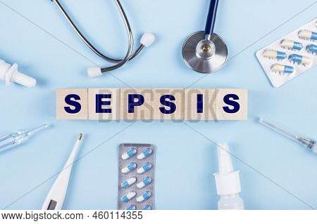 On A Blue Background, A Stethoscope, A Thermometer, Other Medicines And Wooden Cubes With The Text S
