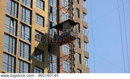 Kyiv, Ukraine - 24.04.2019: Worker Move Down On The Construction Elevator Lift. Blue Sky Background.