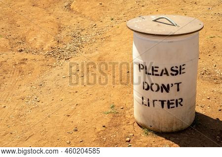 White Trash Bin With The Lid And With The Sign Do Not Litter On Orange Clay Soil