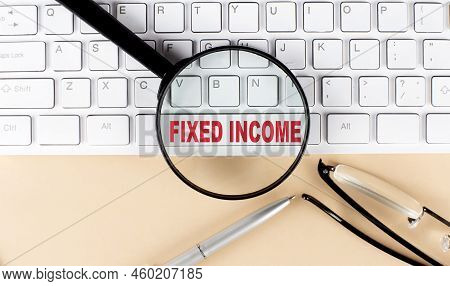 Text Fixed Income On Keyboard With Magnifier , Glasses And Pen On A Beige Background