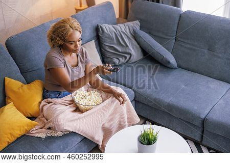 High Angle View Of Woman Sitting On Living Room Couch, Bored At Home Swithcing Channels Using Remote