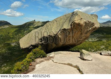 A Huge Granite Monolith Hangs On The Edge Of A High Cliff Overlooking A Picturesque Valley.