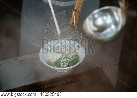 Hands Of Seller Pouring Into The Bowl Of Boiled Noodles