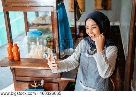 Excited Woman Wearing Apron Looking At Cell Phone While Selling